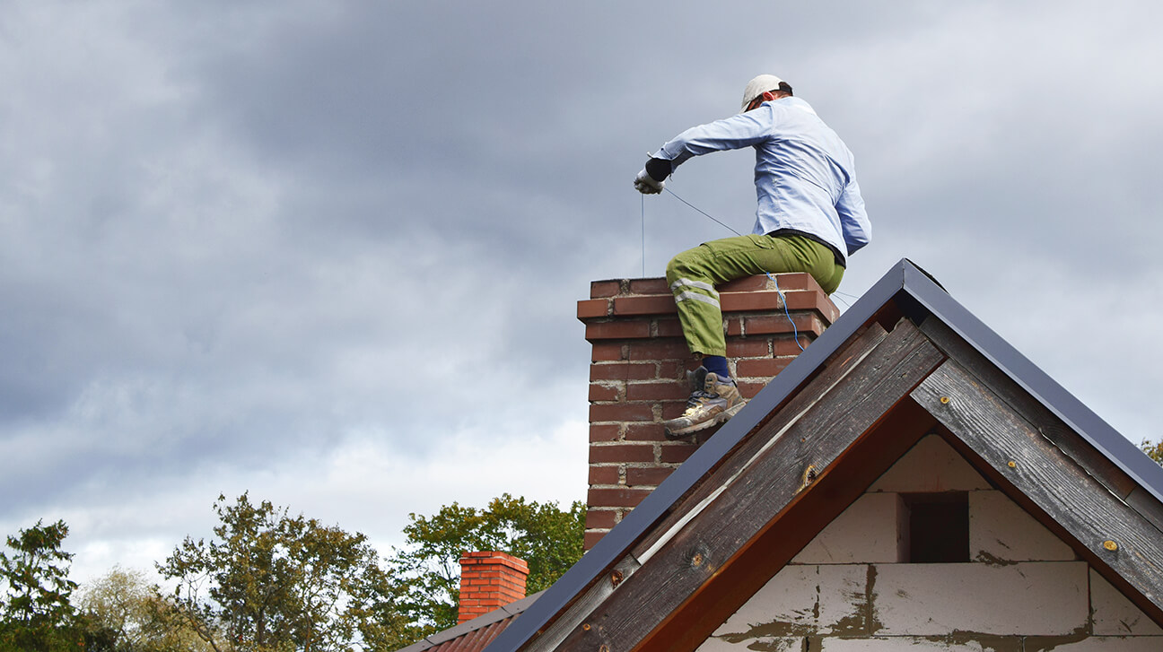 worker on roof cleaning chimney
